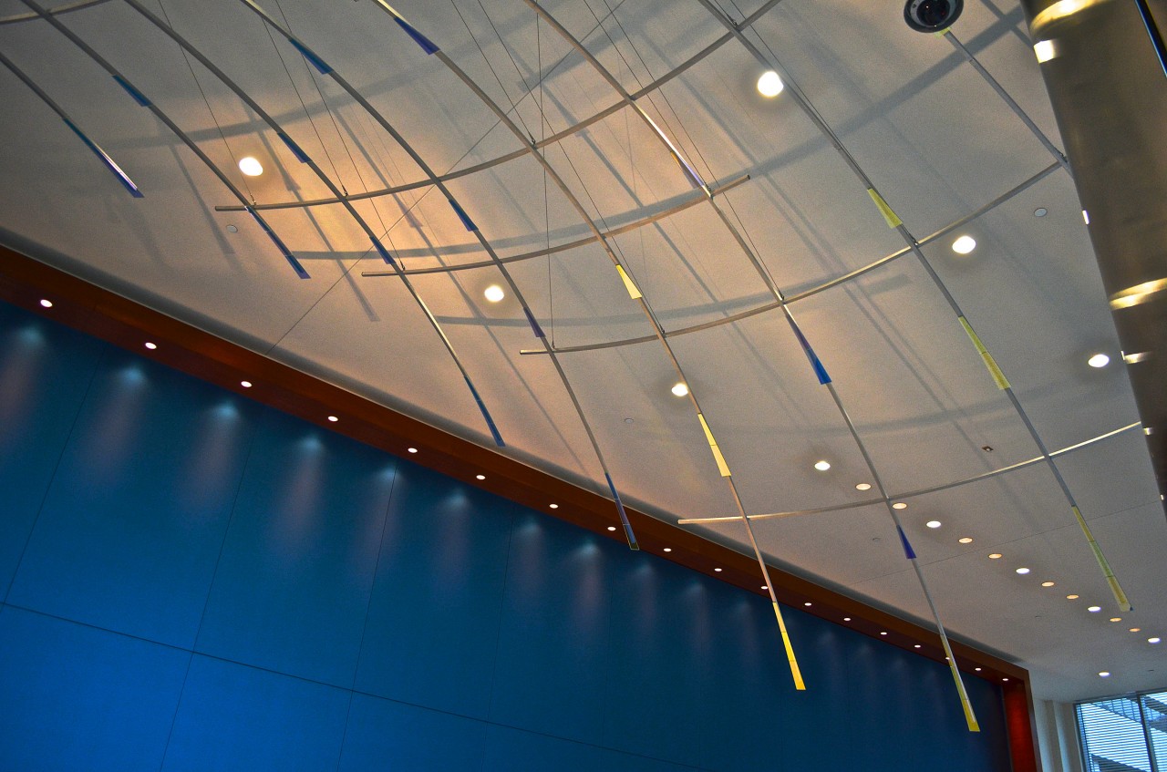 Ed Carpenter’s Radius suspended ceiling sculpture emanates outward through the Ann Arbor Justice Center lobby. Concealed lighting illuminates laminated glass and polished aluminum details, casting glowing projections of the sculpture’s expansive forms. | Image 5 | Ed Carpenter, Artist