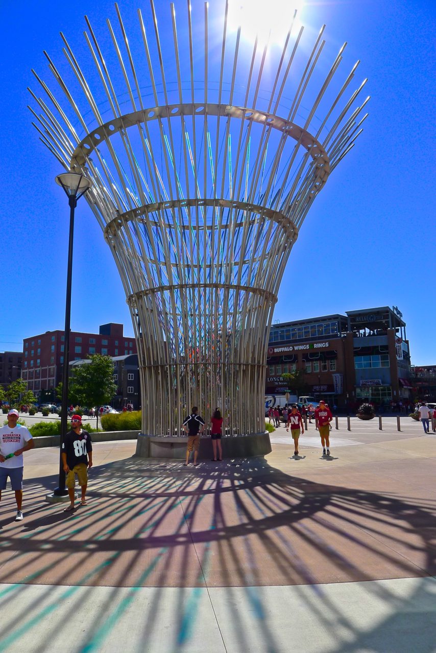 Harvest monumental public sculpture in Lincoln, Nebraska day view, showing colored dichroic glass patterns and projections on the plaza with the bright blue Nebraska sky as a backdrop. | Image 7 | Ed Carpenter, Artist