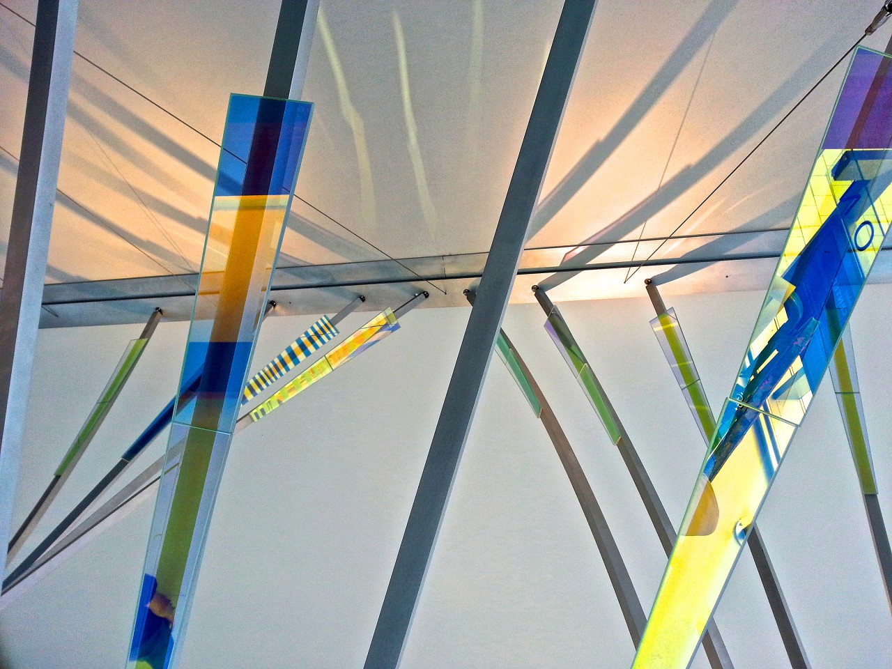 Ed Carpenter’s Radius suspended ceiling sculpture emanates outward through the Ann Arbor Justice Center lobby. Concealed lighting illuminates laminated glass and polished aluminum details, casting glowing projections of the sculpture’s expansive forms. | Image 6 | Ed Carpenter, Artist