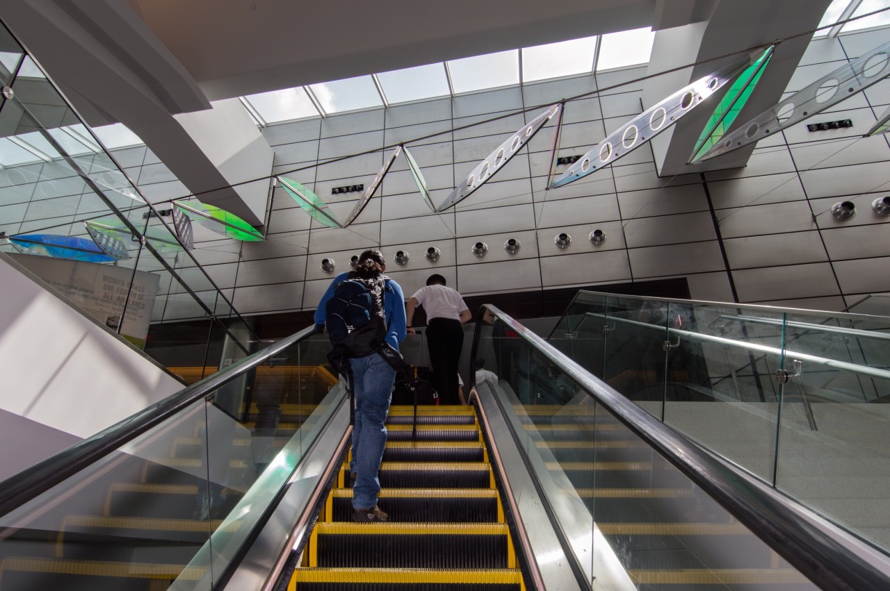 View from the escalator of Ed Carpenter’s Wichita Dwight D. Eisenhower National Airport signature sculpture Aloft delighting travelers with colorful laminated safety dichroic glass above. | Image 9 | Ed Carpenter, Artist